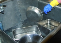 A person rinsing the dishes in the second compartment sink.
