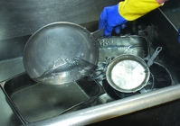 A person placing the rinsed dishes into the third compartment sink.