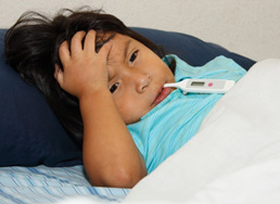 Photo of boy in bed with a thermometer in his mouth