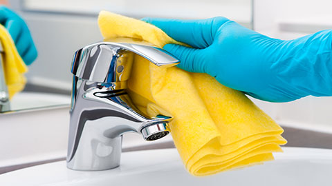 Photo of person wearing gloves disinfecting a faucet