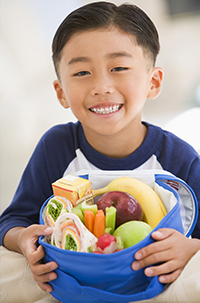 A child holding a lunch box full of healthy food, such as fruits, vegetables, and a wrap.