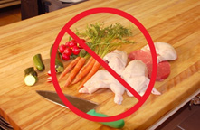 Photo of raw chicken on a cutting board with fruits and vegetables, overlaid by a circle/cross
